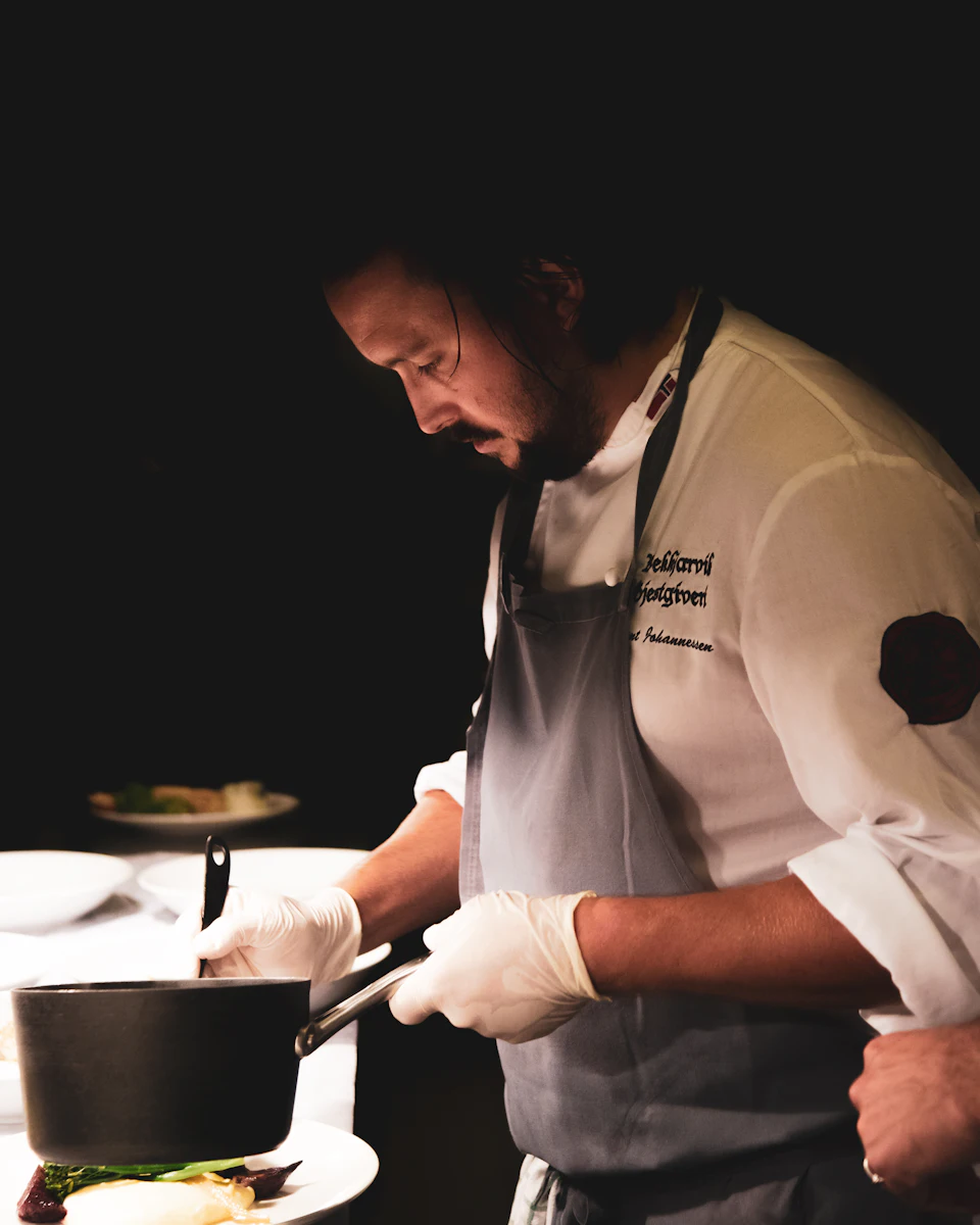 A chef plating food in a dark professional kitchen