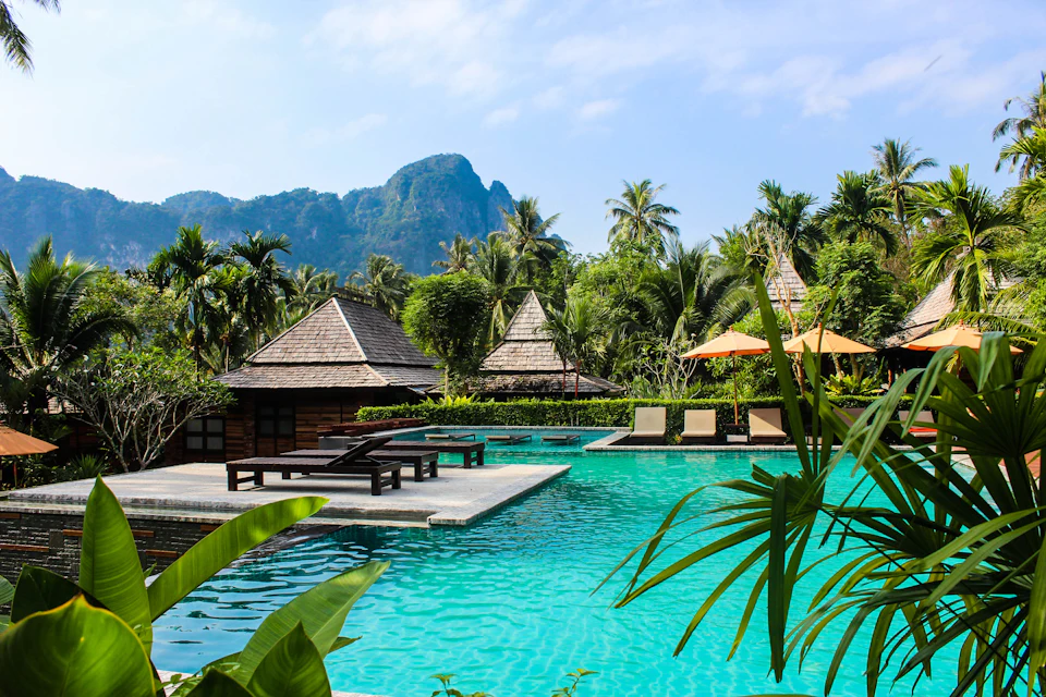 A tropical resort pool with thatched villas beneath limestone mountains